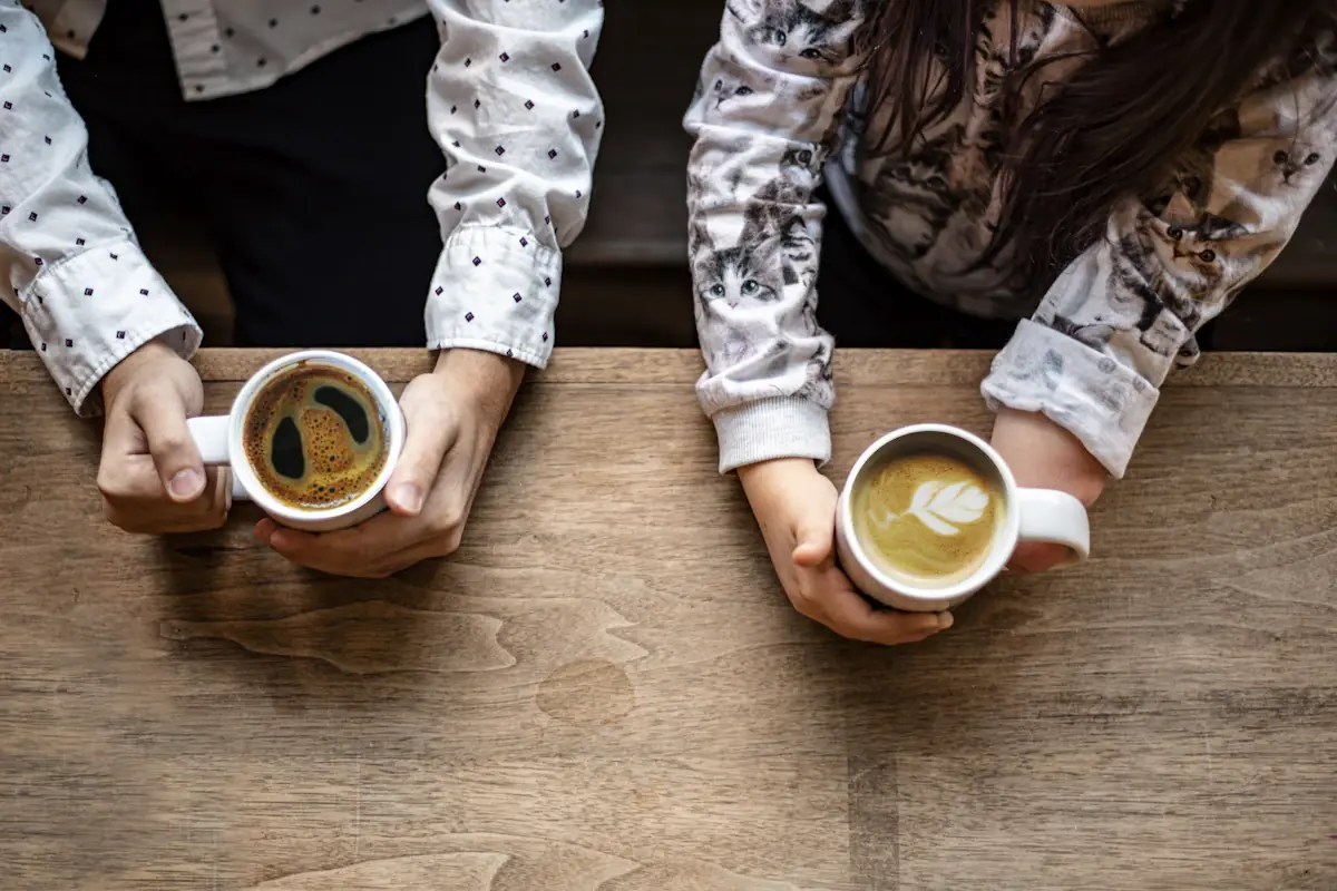 Dos personas conversando con una taza de café en una mesa de madera